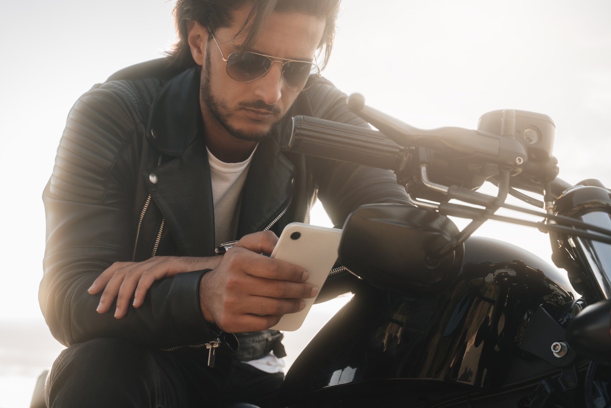 Biker holding his phone, using app to find the best route, sitting on moto bike