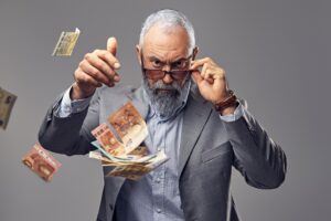 Rich elderly man throwing money against grey background