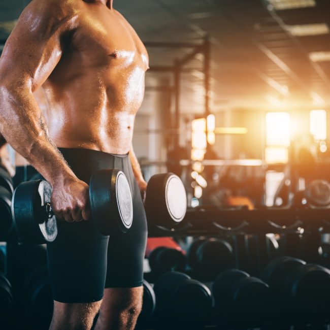 Muscular man holding dumbbels in a gym.