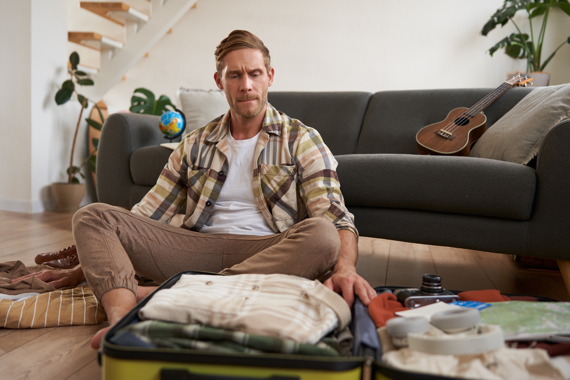 Travelling and tourism concept. Happy young man, sits on floor with luggage opened, packing