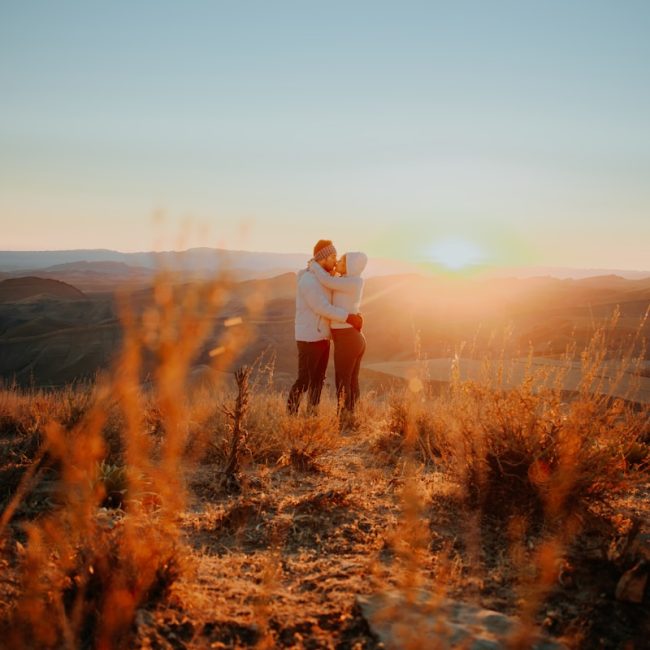 a man and woman standing on top of a grass covered hillside